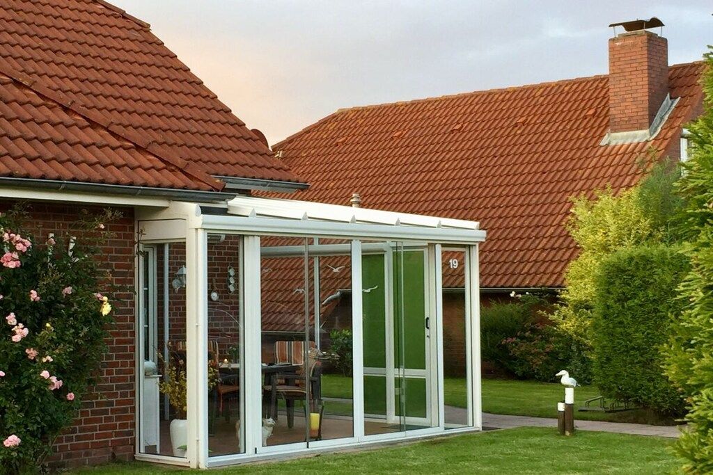 A conservatory with glass doors, a brick house, and a red-tiled roof.