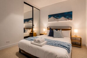 A hotel room with a large bed, two bedside tables with lamps, a mirror, and a painting of mountains. - Docklands 2 Bedroom Hideaway (Docklands)