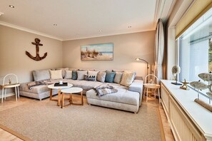 A living room with a sectional sofa, a coffee table, and a painting on the wall. - Holiday apartment with 2 bedrooms (Wenningstedt)