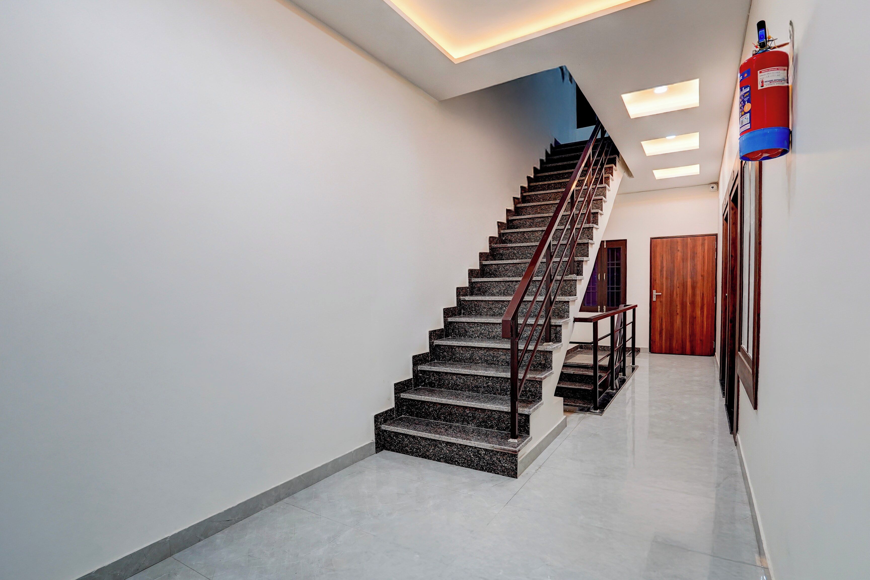 Una escalera moderna con barandilla de metal, que lleva a un rellano con una puerta de madera.