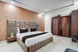 Un dormitorio moderno con una cama grande, cabecera de madera, mesita de noche, planta en maceta y armario.