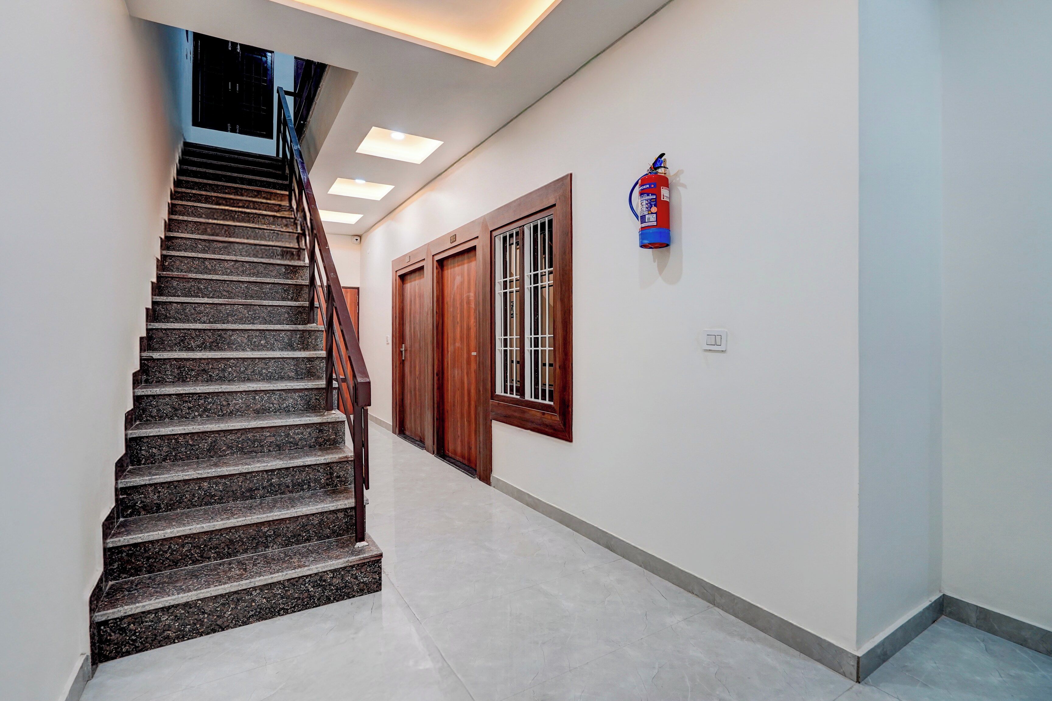 A staircase with a handrail leading to a landing, a fire extinguisher mounted on the wall, and a door with a window.