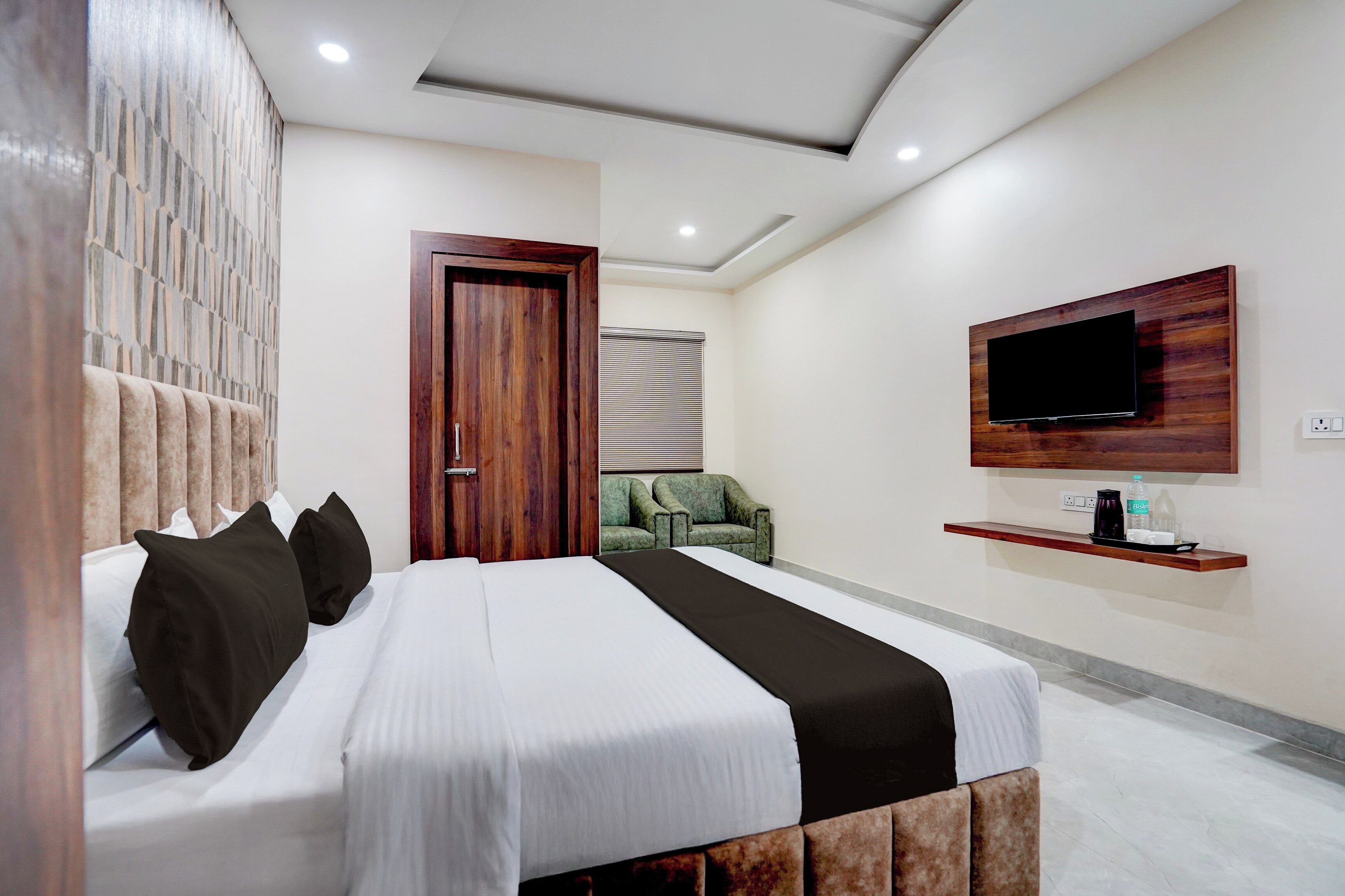 A modern hotel room with a large bed, a television mounted on the wall, and a seating area with a chair.