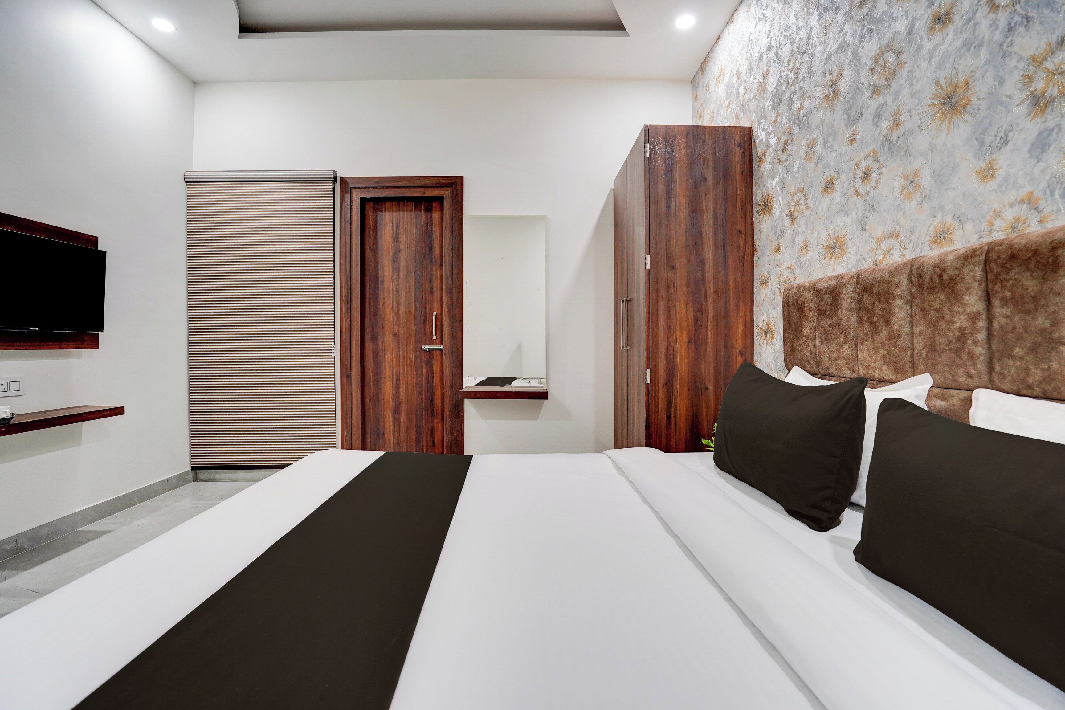 A modern bedroom with a large bed, wooden wardrobe, and a television mounted on the wall.