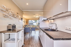 A modern kitchen with a central island, a dining area with chairs, and a view to the outside. - Apartment with 1 bedroom (Wenningstedt)