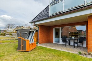 A modern house with a patio area, a barbecue grill, and a glass door leading to a covered outdoor space. - Apartment with 1 bedroom (Wenningstedt)