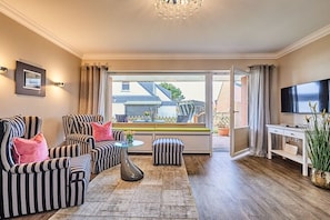 A living room with striped sofas, a coffee table, a TV, and a view of the outside. - Apartment with 1 bedroom (Wenningstedt)