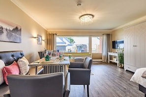 A modern living room with a dining area, a large window with curtains, a chandelier, and a television. - Apartment with 1 bedroom (Wenningstedt)