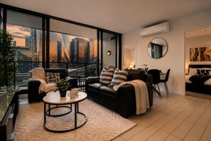A modern living room with a city view, a round coffee table, and a black leather sofa. - Docklands Rooftop Pool Retreat (Docklands)