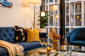 A modern living room with a blue sofa, a glass coffee table, and a decorative vase with flowers. - Blue Haven Docklands 2 Bedroom (Docklands)