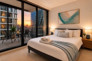 Ein modernes Hotelzimmer mit einem großen Bett, einem Balkon mit Tisch und Stühlen und Blick auf die Stadt.