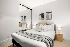Ein modernes Schlafzimmer mit einem großen Bett, Nachttischen, einem Spiegel und abstrakter Wandkunst.