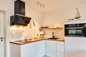 A modern kitchen with white cabinetry, a wooden countertop, a black range hood, a coffee machine, and a small sailboat decoration. - Holiday apartment with 1 bedroom (Archsum)