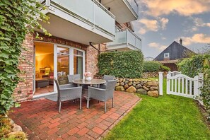 A house with a patio area featuring a table and chairs, a stone wall, and a white picket fence. - Holiday apartment with 2 bedrooms (Westerland)