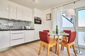 A modern kitchen with white cabinets, a black countertop, and a dining area with a glass table and red chairs. - Holiday apartment with 2 bedrooms (Hörnum)