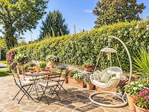 Eine Terrasse im Freien mit einem runden Tisch, Stühlen, einer Hängesessel und Topfpflanzen.