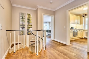 A modern interior with a wooden floor, a staircase with a railing, and a kitchen area visible through an open doorway. - Holiday apartment with 3 bedrooms (Wenningstedt)