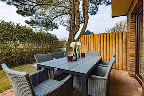 An outdoor dining area with a table and chairs, surrounded by a wooden fence and greenery. - Holiday apartment with 3 bedrooms (Wenningstedt)