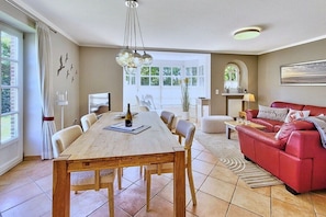 Amplia sala de estar con una mesa de comedor, sofá rojo y vistas al exterior.