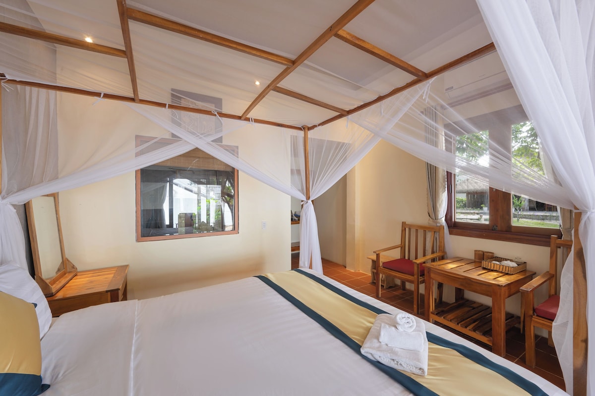 Una habitación con cama, una mesa y sillas, con mosquitero sobre la cama.