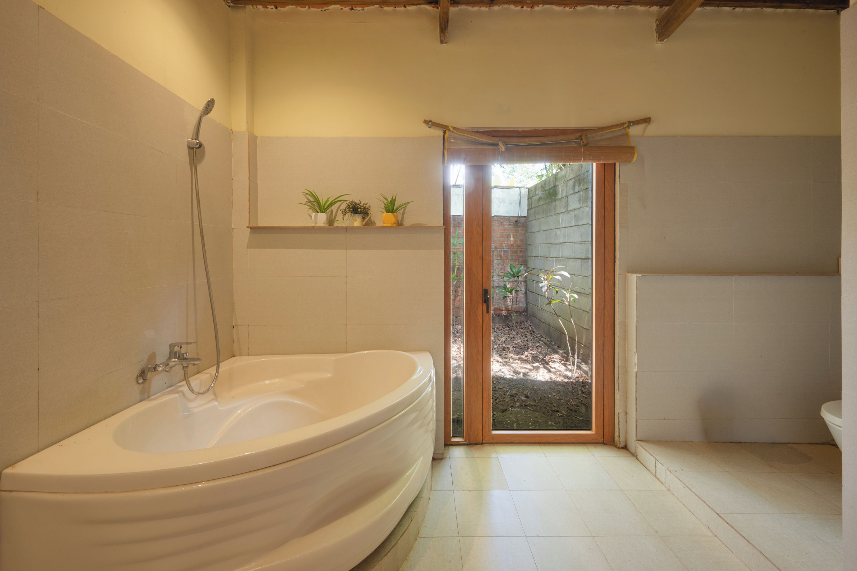 Un baño con bañera, ducha, inodoro y una pequeña repisa con plantas.