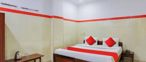 A hotel room with a bed, bedside table, and a small table with a kettle and glasses.
