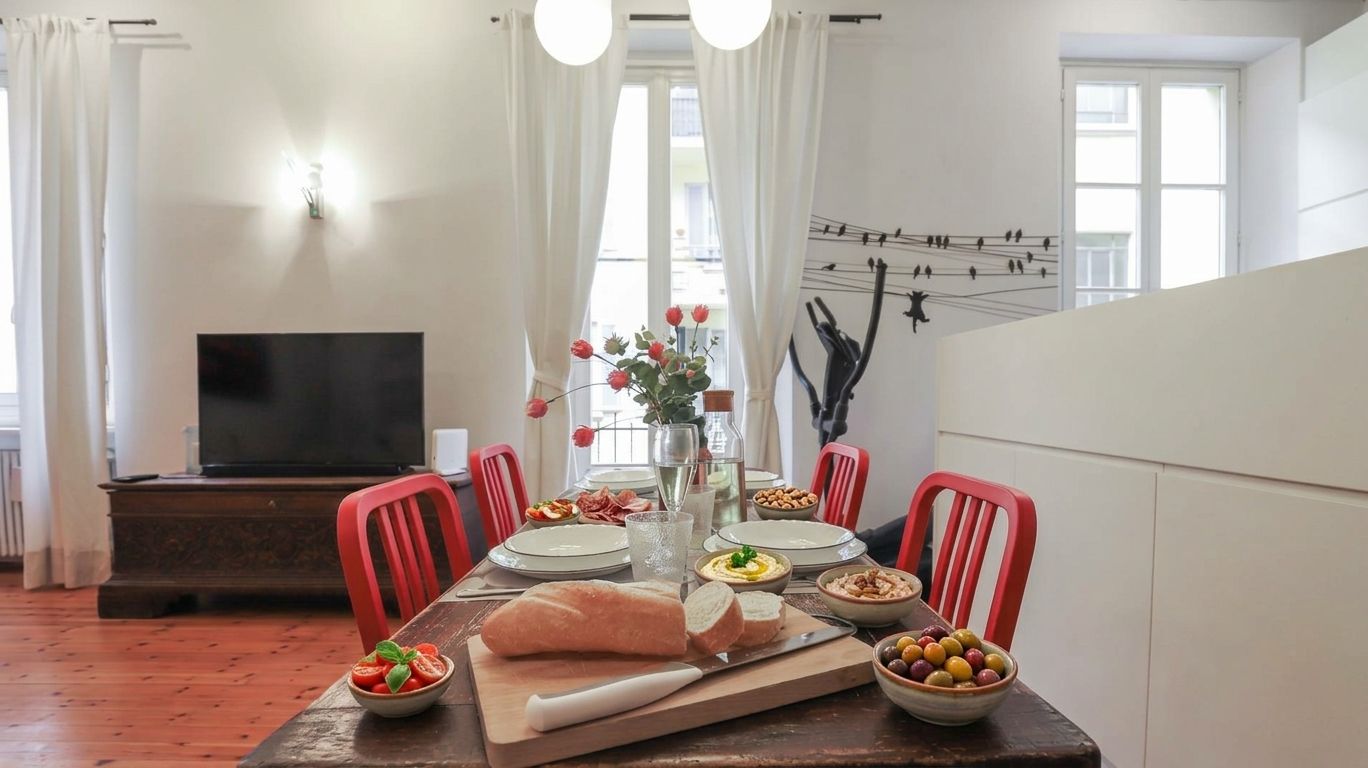Un comedor con una mesa de madera, sillas rojas, un televisor y una pared con un mural de pájaros.