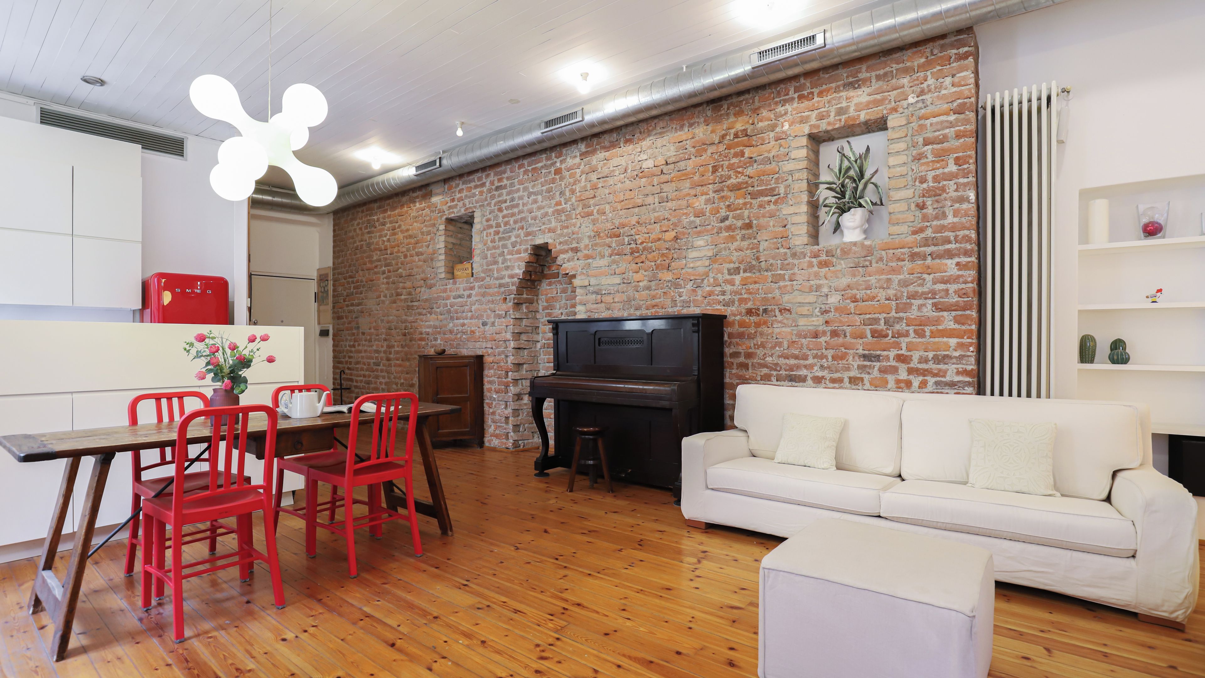 Una sala de estar con pared de ladrillo, un piano, un sofá blanco y sillas rojas.