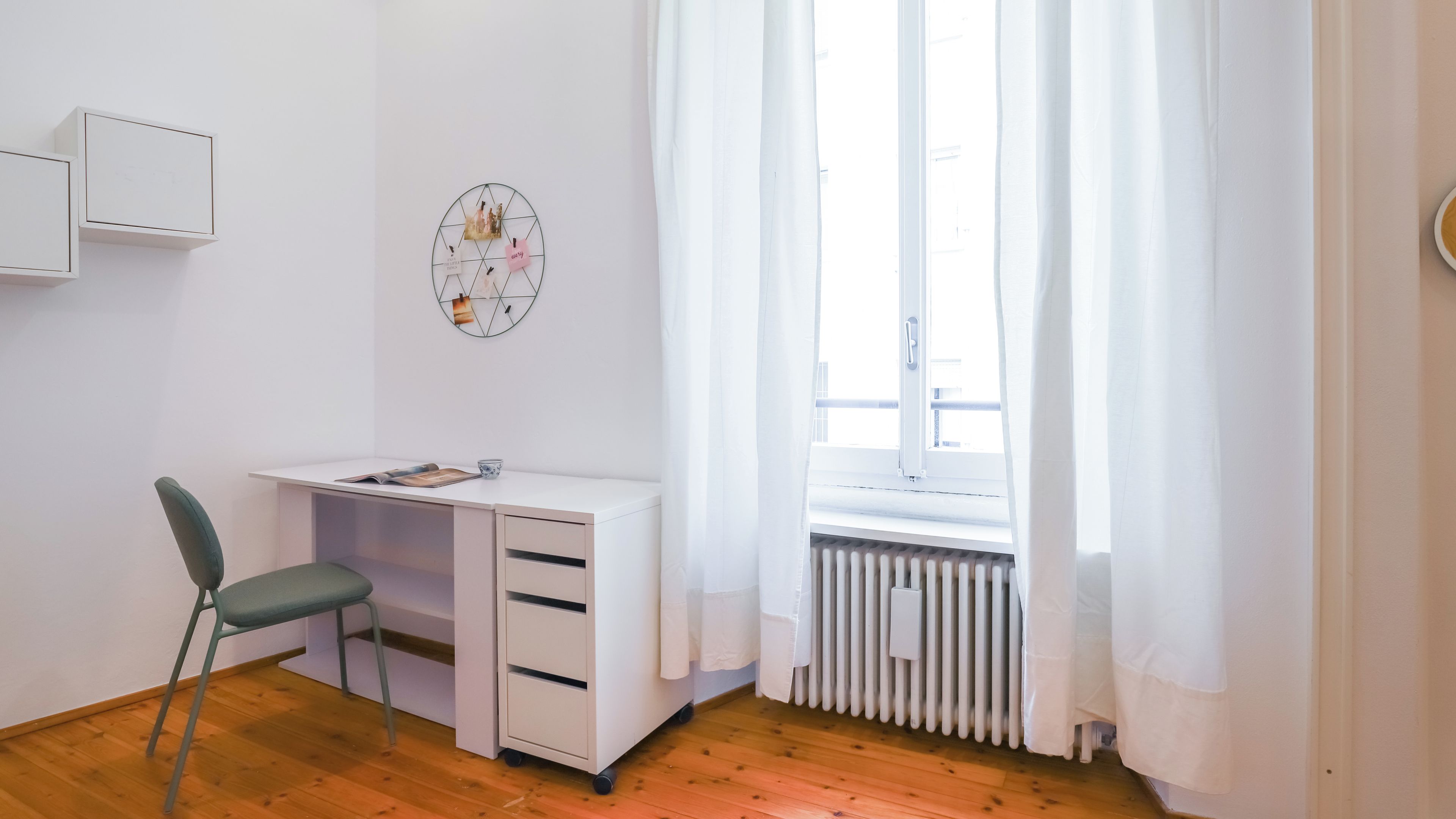 Una habitación con escritorio, silla, radiador y ventana con cortinas.