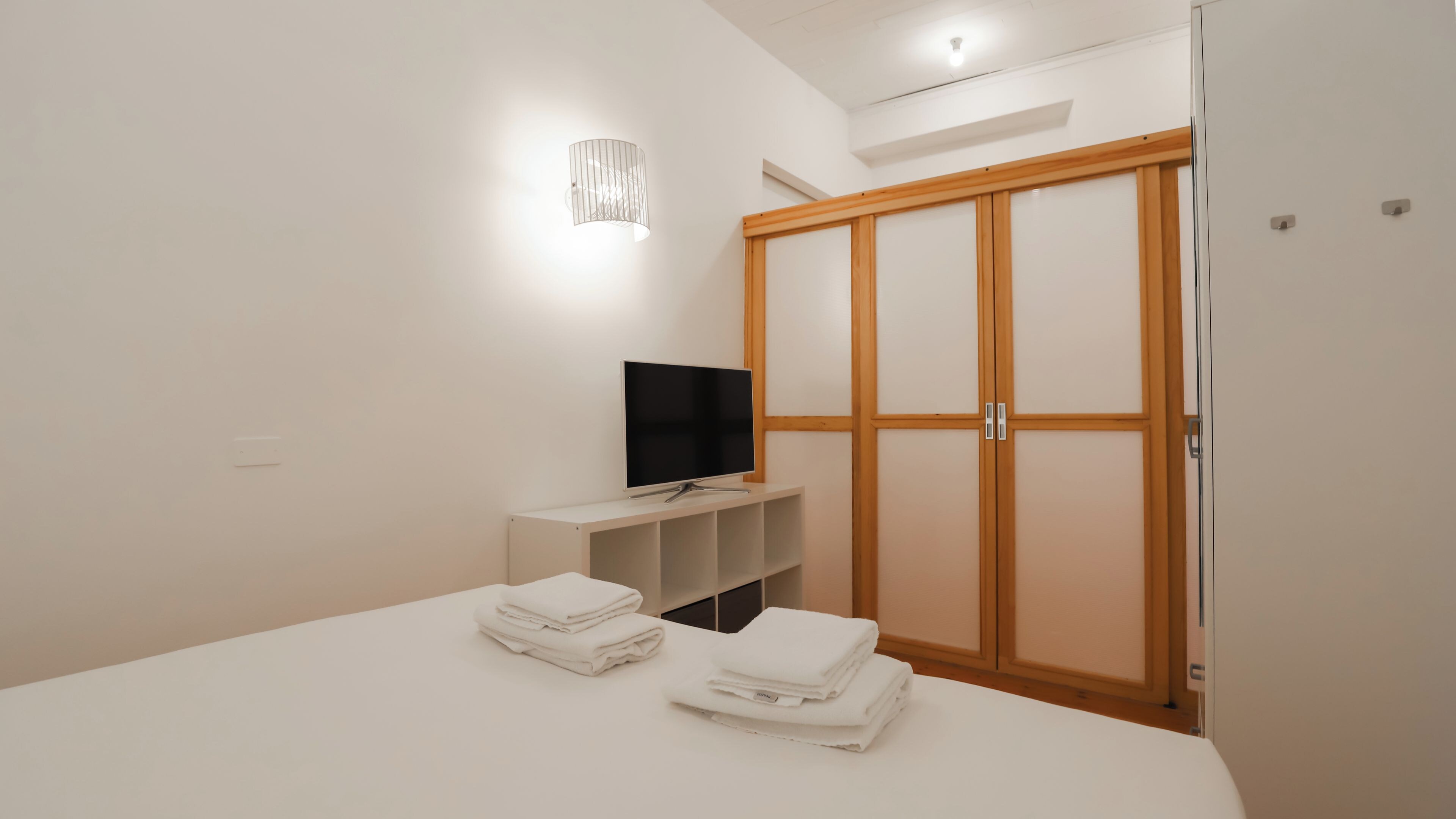 Un dormitorio con cama, televisor, armario y estantería.