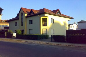 Ein zweigeschossiges Wohnhaus mit rotem Ziegeldach, einem kleinen Balkon und einem befestigten Eingangsbereich.