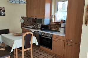 Eine kompakte Küche mit Holzausstattung, einer Mikrowelle, einem Backofen und einem Essbereich mit Tisch und Stühlen.