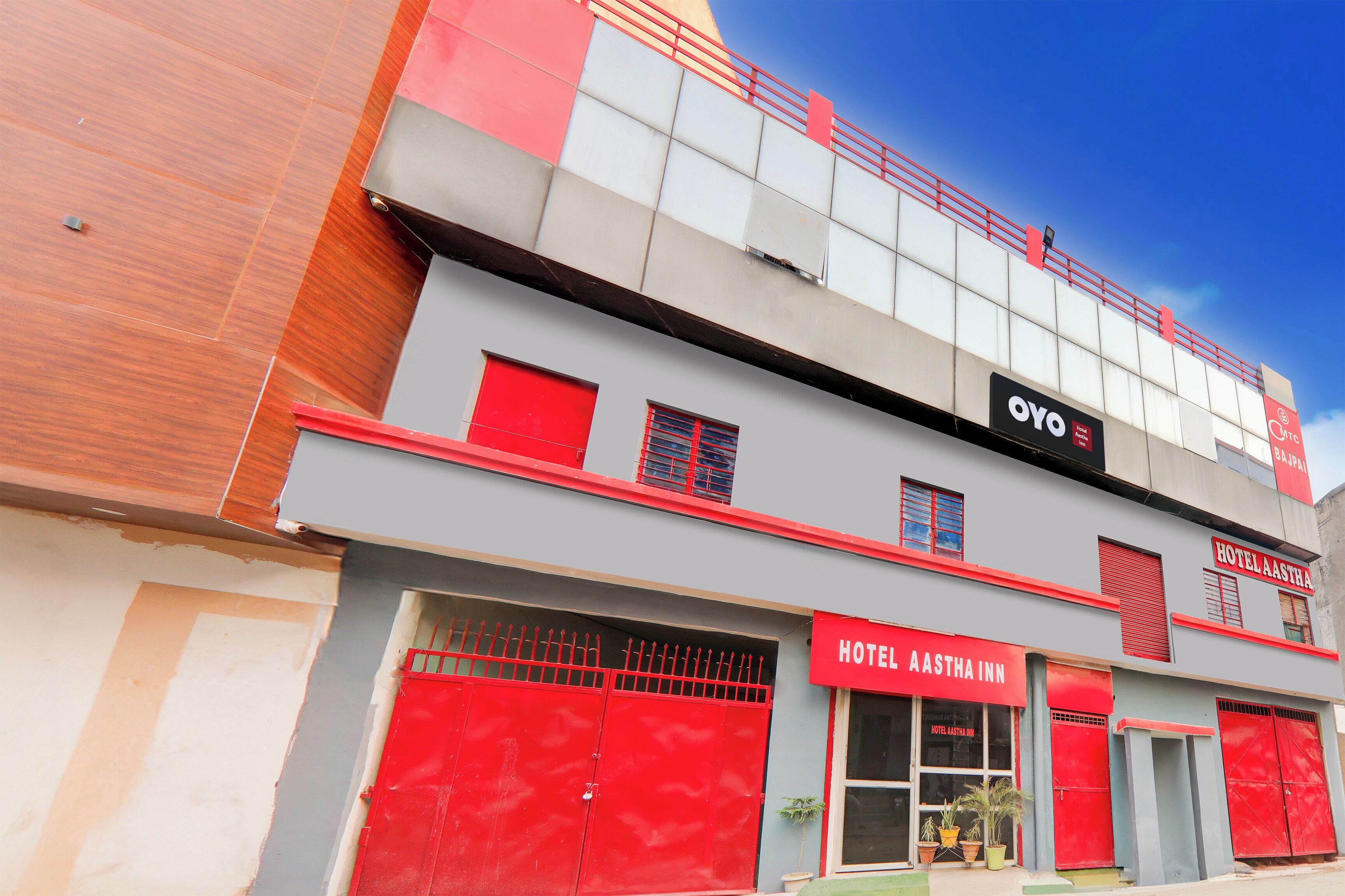 Un hotel con fachada roja y gris, un llamativo letrero que dice 'HOTEL AASTHA INN' y una puerta roja.