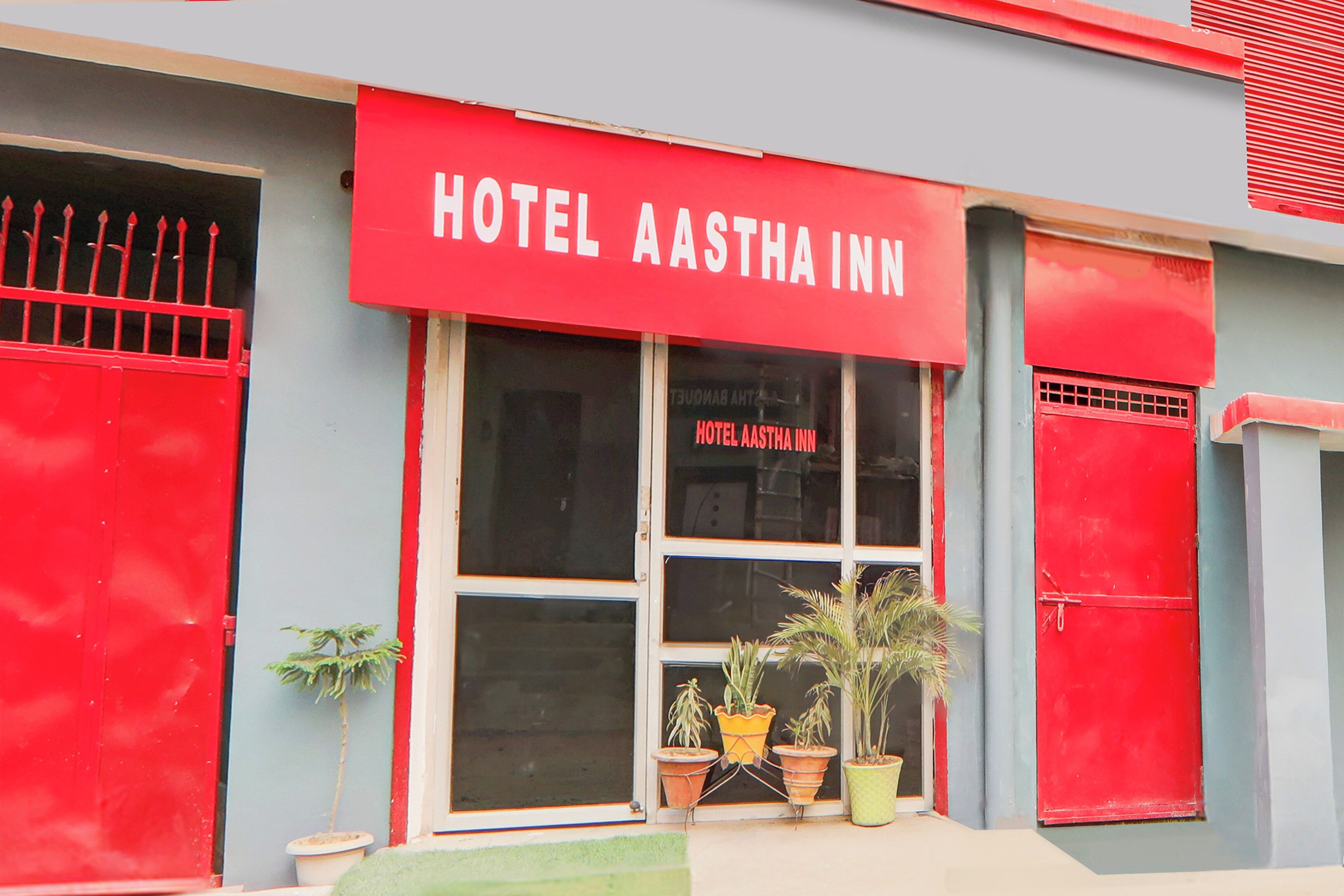 Un bâtiment doté d’une marquise rouge sur laquelle on peut lire « HÔTEL AASTHA INN » et d’une fenêtre portant le même nom.