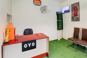 Un área de recepción con un escritorio identificado con 'OYO', un televisor montado en la pared y dos sillas.