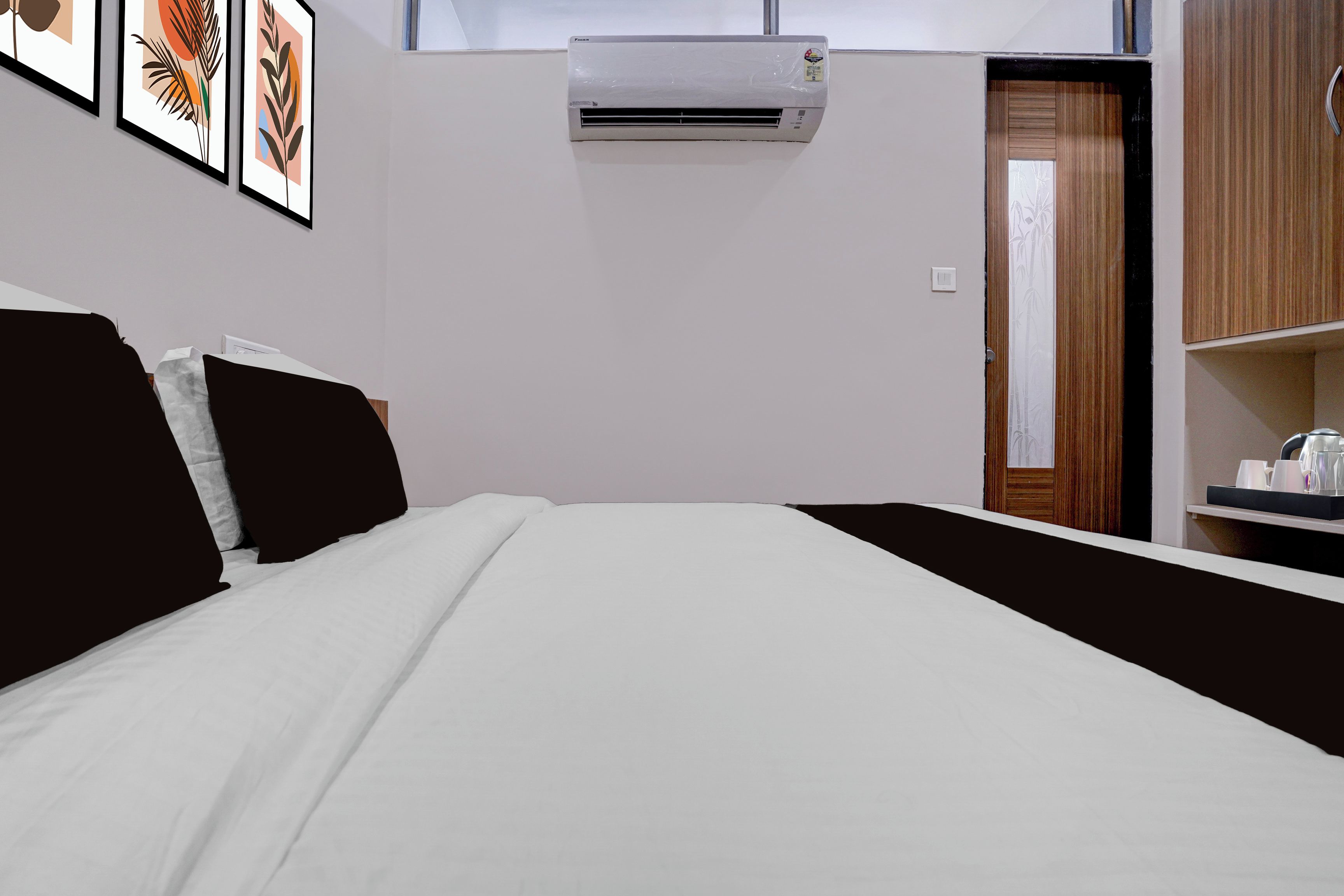Une chambre d’hôtel avec un lit, un climatiseur fixé au mur, une porte avec un panneau en bois et une petite table sur laquelle se trouve un plateau avec divers objets.