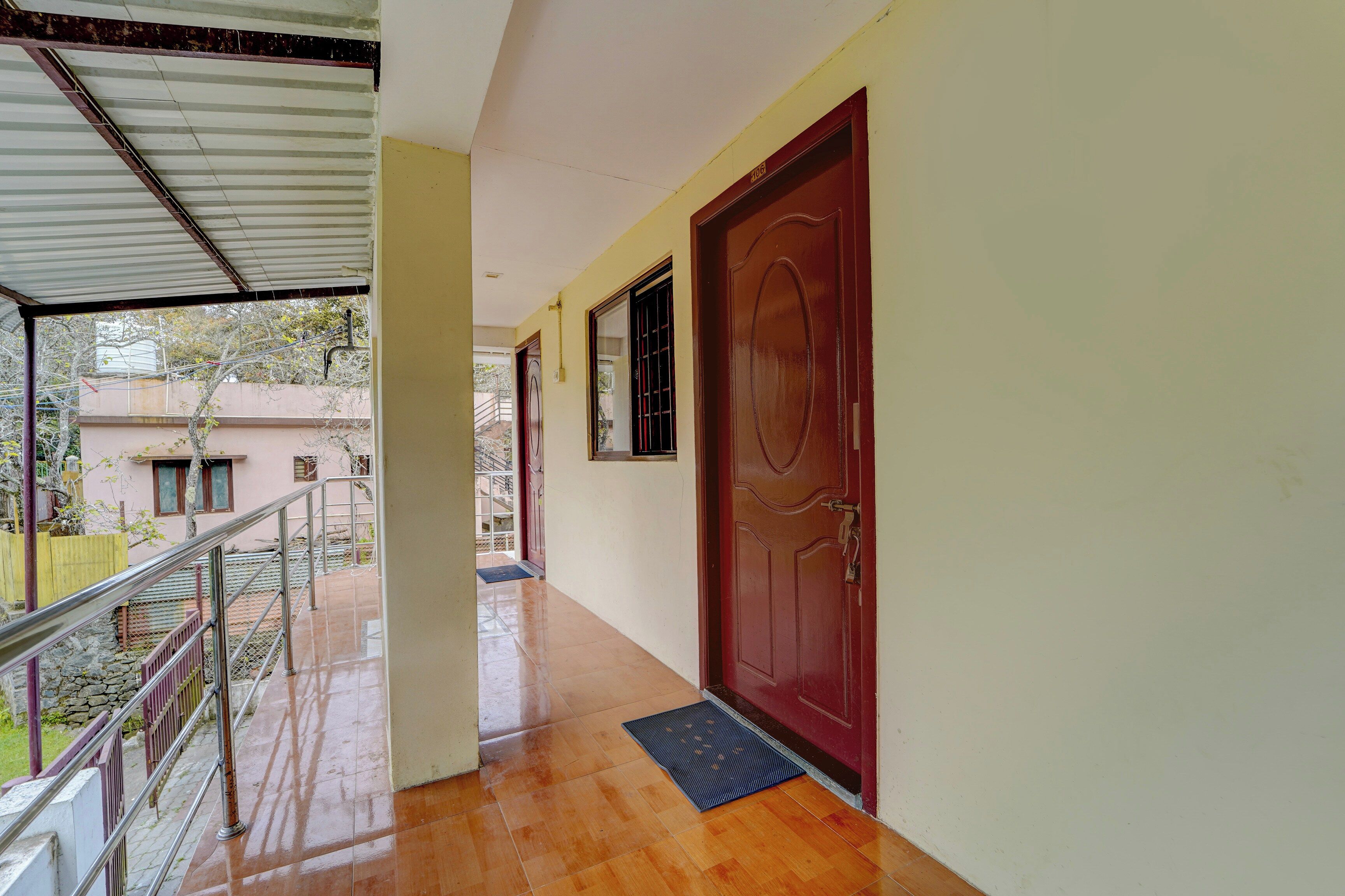 A corridor with a red door, a metal railing, and a tiled floor.