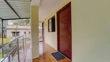 A corridor with a red door, a metal railing, and a tiled floor.
