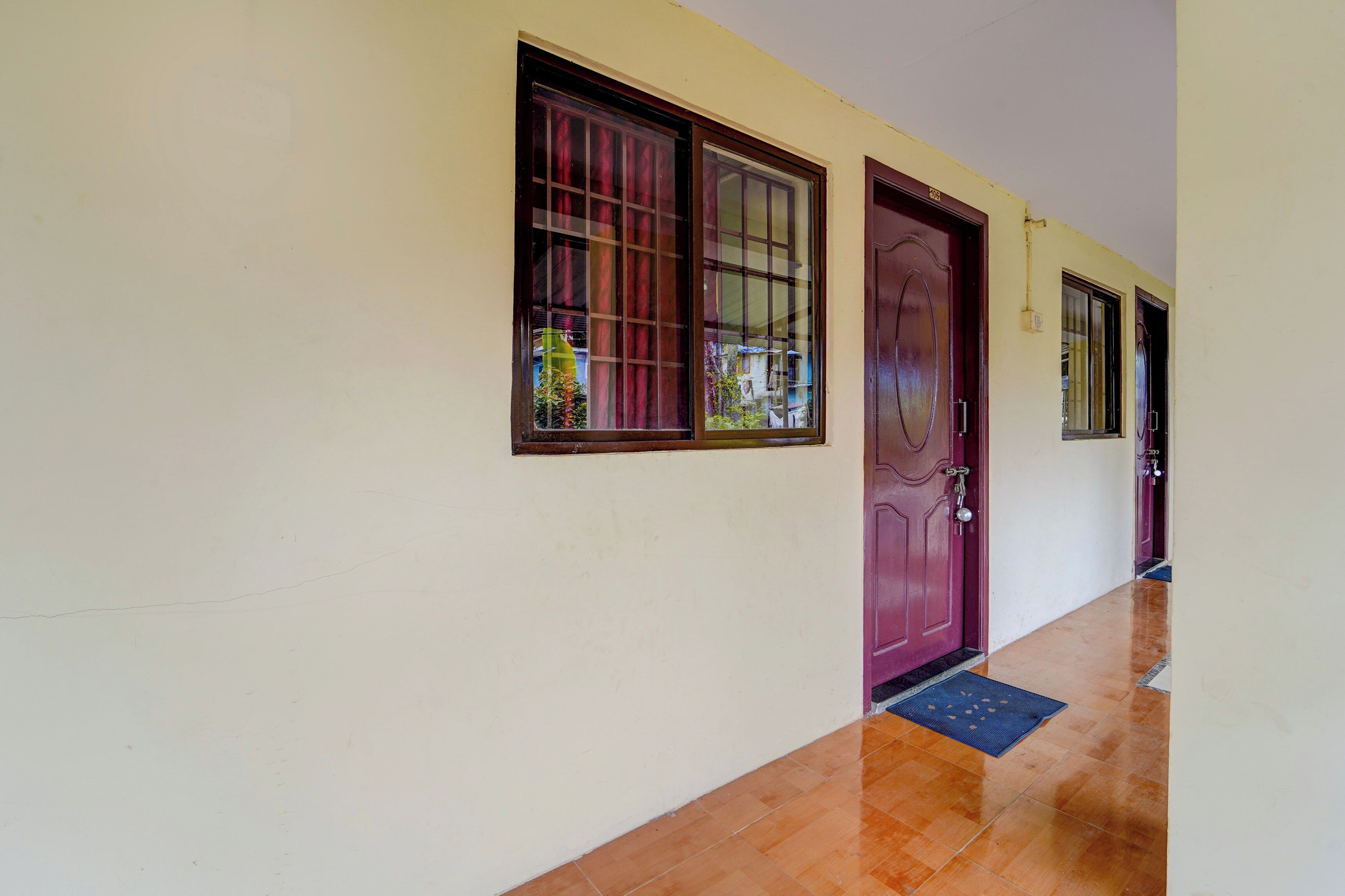 A hallway with a wooden floor, a purple door, and windows with metal bars.