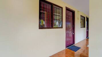 A hallway with a wooden floor, a purple door, and windows with metal bars.
