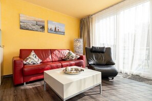 A room with a red leather sofa, a black leather armchair, a white coffee table, and two paintings on the wall. - Holiday apartment Villa Patricia 319558 (Kühlungsborn-Ost)