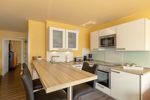 A compact kitchen with white cabinets, a wooden dining table, and a built-in oven. - Holiday apartment Villa Patricia 319558 (Kühlungsborn-Ost)