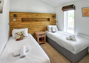 Une chambre avec deux lits, une tête de lit en bois, du linge de lit blanc et une petite table de chevet.