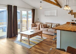 Un vaste espace de vie comprenant une table basse en bois, un ensemble de canapés et un coin cuisine doté d’un plan de travail en bois.