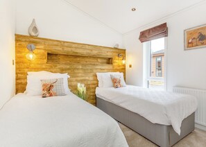 A hotel room with two beds, wooden headboard, wall-mounted lights, and a window with a view. - 1 bedroom accommodation in Fort Augustus (Fort Augustus)