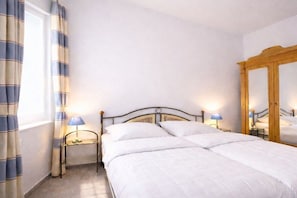 Ein Schlafzimmer mit einem Bett, Nachttischlampen, einem Spiegel und Vorhängen.