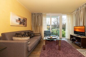 A living room with a sofa, a glass coffee table, a television, and a view of the outdoors through a sliding glass door. - Holiday apartment Villa Patricia 319556 (Kühlungsborn-Ost)