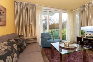 A living room with a sofa, a blue armchair, a glass coffee table, and a television on a stand. - Holiday apartment Villa Patricia 319556 (Kühlungsborn-Ost)