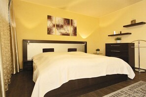 A bedroom with a bed, a nightstand, a dresser, a wall-mounted shelf with a plant, and a painting above the bed. - Holiday apartment Villa Patricia 319555 (Kühlungsborn-Ost)