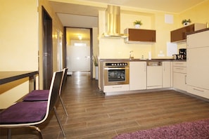 A modern kitchen with a built-in oven, a dishwasher, and a stainless steel range hood. There is a purple chair and a wooden floor. - Holiday apartment Villa Patricia 319555 (Kühlungsborn-Ost)